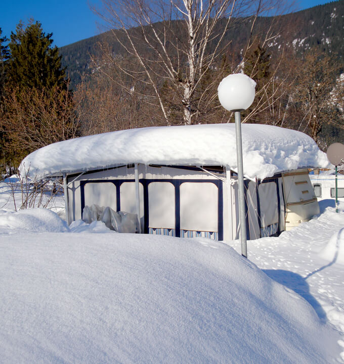 Wohnwagen und Vorzelt unter Schutzdach im Winter mit dicker Schneedecke