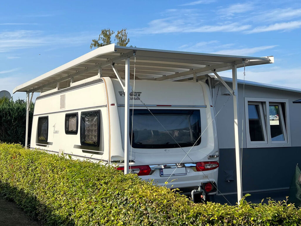 Wohnwagen mit Schutzdach vor einer Hecke auf dem Stellplatz